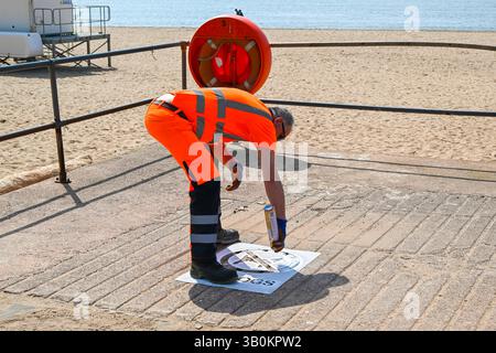 Exmouth, Devon, Großbritannien. April 2025. Wetter in Großbritannien: Ein Mitarbeiter des rates an der Küste malte neue No Dogs Schilder am Eingang zum Strand im Badeort Exmouth in Devon an einem heißen, sonnigen Tag vor dem Hundeverbot vom 1. Mai bis 30. September. Bildnachweis: Graham Hunt/Alamy Live News Stockfoto