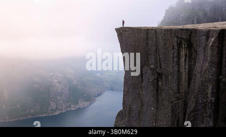 Am Rande von Preikestolen steht eine Einzelfigur, die den atemberaubenden Blick auf den Lysefjord bei Sonnenaufgang in Norwegen genießt Stockfoto