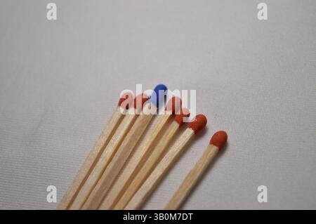 Ein einziger blauer Match hebt sich von mehreren roten Matches ab, die auf einer makellos weißen Oberfläche angeordnet sind. Stockfoto