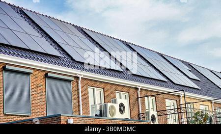 Das moderne Residence verfügt über eine im Freien installierte Luftwärmepumpe und elegante schwarze Solarpaneele, die Sonnenenergie für ein effizientes, umweltfreundliches Leben in den Niederlanden nutzen. Stockfoto