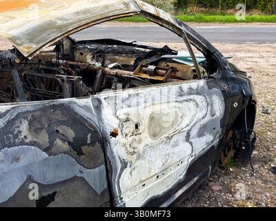 Seitenansicht eines vollständig verbrannten Fahrzeugs mit verzogener und blasenförmiger Farbe, fehlendem Innenraum und rostenden Komponenten nach einem intensiven Brand in der Nähe eines Stockfoto
