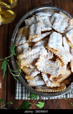 Karnevalszeit. Hausgemachte traditionelle italienische Karnevalsbonbons. Chiacchiere mit Puderzucker bestreut, hölzerner Hintergrund. Direkt darüber. Stockfoto