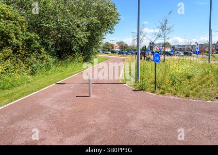 Fahrradweg, der an einem sonnigen Sommertag in einer Küstenstadt in Belgien neben einem Parkplatz verläuft Stockfoto