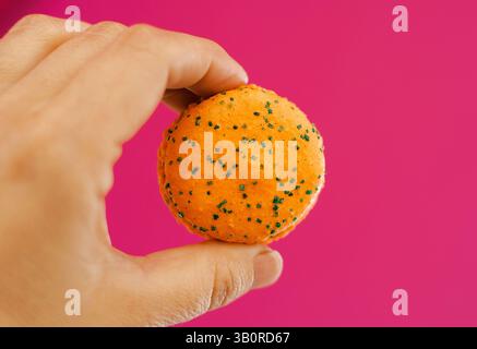 Orange Macarons mit grünen Streuseln in der Hand auf Himbeerhintergrund Stockfoto