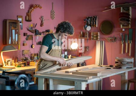 Ernsthafter engagierter Zimmermann, der mit Holzmöbelteilen auf Werkstattbank arbeitet und die Lieferung vorbereitet Stockfoto