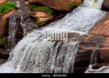 Rauschende Wasserfälle fließen über glatte Felsen in ruhiger Umgebung, umgeben von Grün Stockfoto