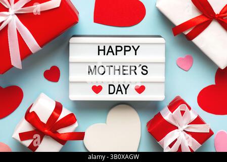 Alles Gute zum Muttertag. Leuchtkasten mit dem Wort Happy Mother's Day neben Herzen und Geschenkboxen auf blauem Hintergrund Stockfoto