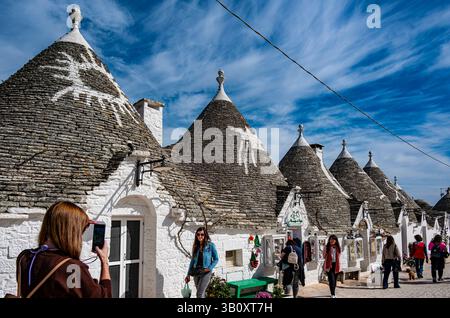 Touristen machen Fotos in der Nähe malerischer Trullihäuser in Alberobello, Apulien Stockfoto