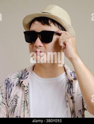 Asiatischer Mann mit tropischem Hemd, Strohhut und Sonnenbrille. Mode- und Lifestyle-Konzept für den Sommer. Stockfoto