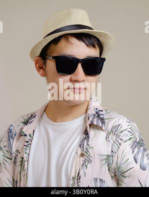 Asiatischer Mann mit tropischem Hemd, Strohhut und Sonnenbrille. Mode- und Lifestyle-Konzept für den Sommer. Stockfoto
