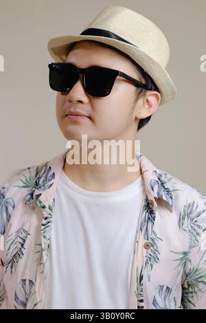 Asiatischer Mann mit tropischem Hemd, Strohhut und Sonnenbrille. Mode- und Lifestyle-Konzept für den Sommer. Stockfoto