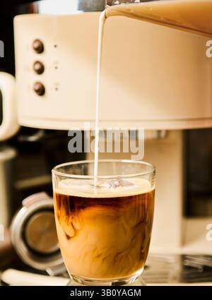 Cremiger Eiskaffee wird in Glas mit Espresso-Maschine im Hintergrund gegossen Stockfoto