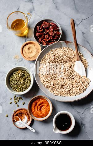 Eine Auswahl an Zutaten für ein Müsli-Rezept, einschließlich Hafer, Pekannüsse, Kürbispüree, Kürbiskerne, brauner Zucker, Gewürze, Ahornsirup und Öl auf Stockfoto