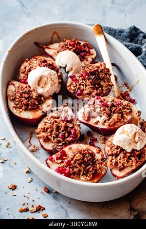 Gebackene Äpfel, garniert mit Granola Crumble und Eis, garniert mit Granatapfelkernen in einer weißen Schale. Stockfoto