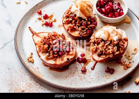 Gebackene Birnen mit einer Müslimischung, Eis und Granatapfelkernen serviert auf einem Teller. Stockfoto