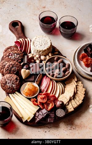 Eine Auswahl an Snacks einschließlich Keksen, Käse, Obst, Schokolade und Gläsern Rotwein, die wunderschön auf einem Holzbrett angeordnet sind. Stockfoto