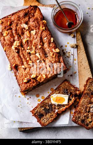 Ein Stück Bananenbrot mit Walnüssen und Honig, begleitet von einer Scheibe mit Butter und Honig. Stockfoto