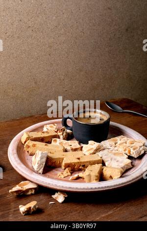 Traditionelles spanisches Dessert klassisches weiches Orangenturron und knuspriges Mandelturron, in Stücke geschnitten auf rustikaler Tonplatte. Espresso in schwarzer Tasse, Holz Stockfoto