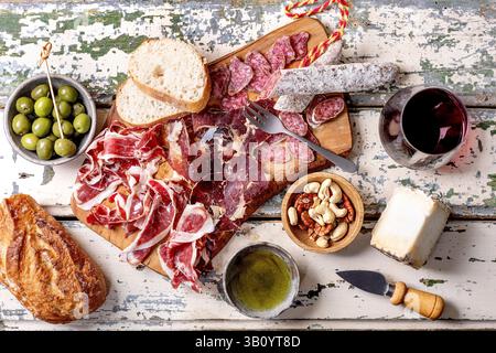 Snackbrett mit traditionellem spanischen Jamon Iberico, in Scheiben geschnittener Fuet-Wurst, Käse, grünen Oliven, weißem Brot, Nüsse, Olivenöl, Glas Rotwein. Licht Stockfoto