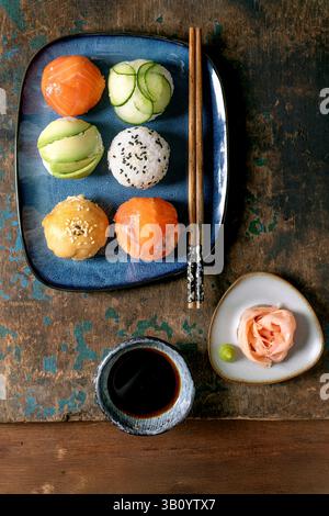 Temari Sushi. Trendige Sushi-Bällchen mit Lachs, Avocado, Gurke und japanischem Omelett auf blauem Teller. Sojasauce, eingelegter Ingwer, Essstäbchen auf rustikalem wo Stockfoto