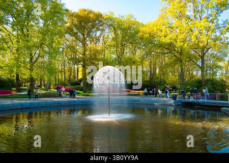 Keukenhof, Niederlande - 2023 - 05 - 02: Besucher bewundern einen modernen kugelförmigen Wasserbrunnen in einem Teich in den Gärten von Keukenhof, Niederlande, umgeben von Stockfoto