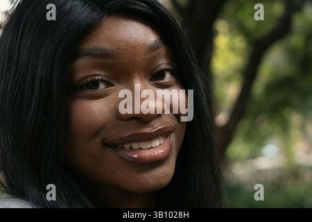Porträt einer schönen jungen afroamerikanerin mit langen schwarzen Haaren, die in einem Park lächelt und einen sonnigen Tag inmitten der Natur genießt Stockfoto