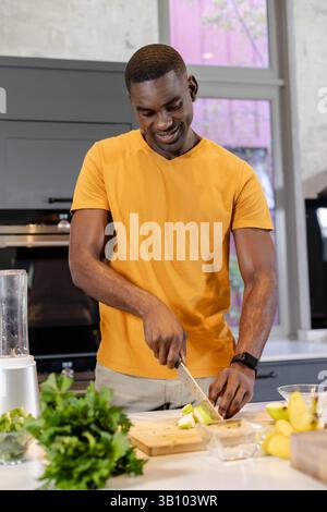 Blattgemüse hacken, afroamerikanischer Mann, der Smoothie auf Kücheninsel mit Mixersockel zubereitet Stockfoto