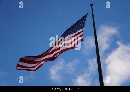 Stolz vor einem klaren blauen Himmel mit hellweißen Wolken winkt eine amerikanische Flagge im Wind; patriotische Nahaufnahme zum Unabhängigkeitstag. Stockfoto