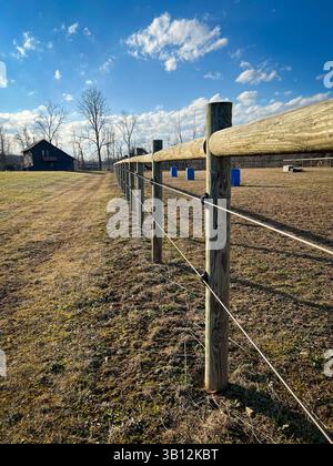 Hölzerner Weidezaun, der über das ländliche Feld in Richtung Scheune unter blauem Himmel führt Stockfoto