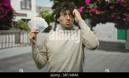 Hispanischer Mann draußen auf der Stadtstraße, der polnische Zloty-Banknoten hält und verwirrt in einer lebhaften städtischen Umgebung aussieht. Stockfoto