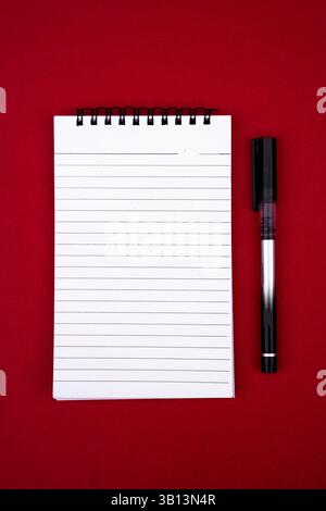 Klare und moderne Draufsicht eines offenen Notebooks und Stifts auf einer leuchtend roten Oberfläche. Perfekt für minimales Design, Arbeitsraumkonzepte oder akademische A Stockfoto