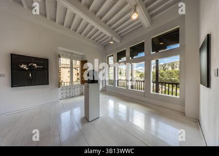 Große Sprossenfenster in einer Halle des Museo de Arte Abstracto Español öffnen sich zu der rauen Felslandschaft der Altstadt von Cuenca, Castilla-La Mancha, Spanien. Eine kleine dunkle Skulptur steht auf einem weißen Podest in der Mitte des Raumes, und ein schwarzes Gemälde hängt an der linken Wand. Calle Canónigos, Cuenca, Castilla-La Mancha, Spanien. Stockfoto