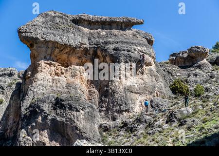 Ein Kletterer erklimmt eine auffällige Felsformation, die einem Hasen ähnelt, auf dem Camino de San Isidro nahe Cuenca, Castilla-La Mancha, Spanien. Zwei weitere Personen sichern und beobachten vom Fuß des Felsens. Stockfoto