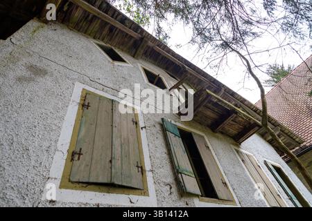 Bad Illstern, italien, verlor seinen Platz. Niedrigwinkelaufnahme eines verwitterten zweistöckigen Gebäudes mit Holzläden, einem kleinen Balkon und Dachschaden, gesehen Agai Stockfoto