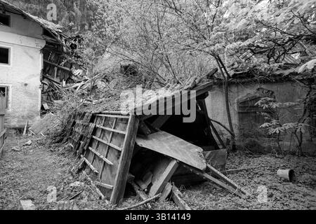 Bad Illstern, italien, verlor seinen Platz. Schwarz-weiß-Bild von baufälligen Gebäuden, darunter ein eingestürzter Schuppen und ein teilweise zerstörtes Haus, umgeben Stockfoto