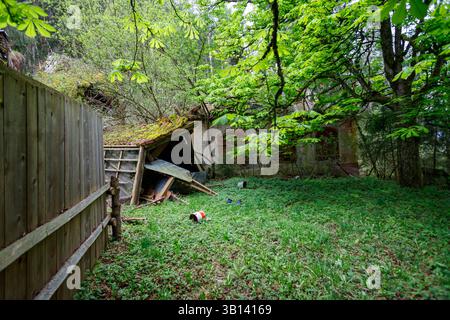 Bad Illstern, italien, verlor seinen Platz. Überwachsener Hof mit baufälligen Schuppen und Ruinen des Gebäudes, begrenzt von Holzzaun und Bäumen. Überwiegend grün Stockfoto