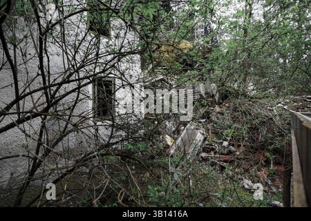 Bad Illstern, italien, verlor seinen Platz. Beschädigtes Gebäude mit Trümmern und bewachsener Vegetation, verdeckt durch Äste, was auf Vernachlässigung oder Abriss hindeutet. Stockfoto