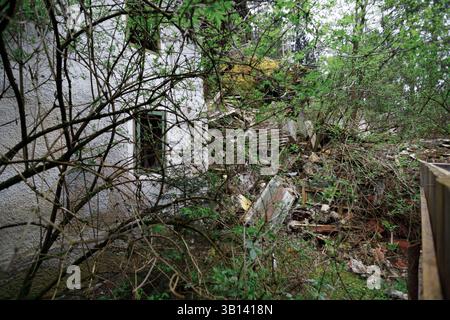 Bad Illstern, italien, verlor seinen Platz. Das Bild zeigt die Seite eines baufälligen Gebäudes mit Fenster, teilweise von Bäumen verdeckt, mit Schutthaufen daneben Stockfoto