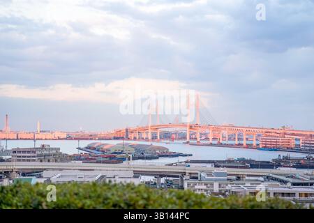 In Minato Mirai, Yokohama, Präfektur Kanagawa, färbt sich eine große Brücke in der Ferne langsam orange im goldenen Glanz der untergehenden Sonne, wodurch ein c entsteht Stockfoto