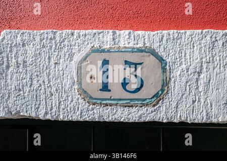 Das alte portugiesische Haus Nr. 13 an der traditionellen Fassade des Colorblock-Gebäudes. Authentischer Adressmarker mit verwitterten Keramikfliesen und blauen Ziffern Stockfoto
