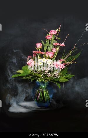 Ein bunter Blumenstrauß in einer Vase auf schwarzem Hintergrund mit Nebeleffekt Stockfoto