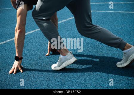Nahaufnahme der Seitenansicht von Mannfüßen in Sportschuhen, die auf der blauen Laufbahn laufen. Starten. Saisontraining, Crossfit und Training. Stockfoto
