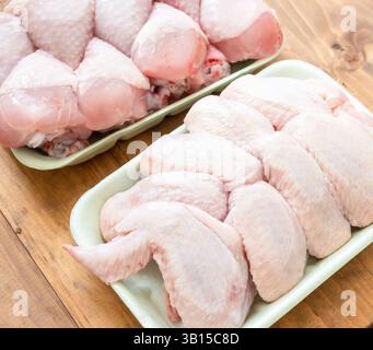 Zwei Tabletts mit Hähnchenflügeln und Beinen sind auf einem Holztisch ausgestellt. Die Flügel werden in Stücke geschnitten und können gekocht werden Stockfoto