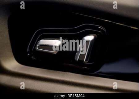 Nahaufnahme des schwarzen Bedienfelds an der Tür eines modernen Autos mit verschiedenen Knöpfen und silbernem Griff vor braunem Lederinnenraum. Stockfoto