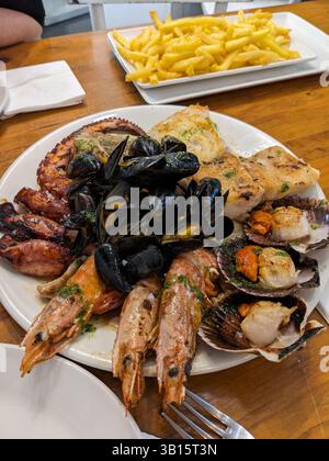 Eine köstliche Platte mit Meeresfrüchten wird mit Pommes frites serviert und bietet ein köstliches und optisch ansprechendes kulinarisches Erlebnis. Das Gericht umfasst gegrillten Oktopus, M Stockfoto