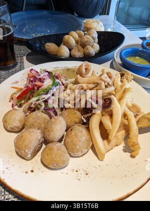 Ein köstlicher Teller mit frittierten Meeresfrüchten, Papas Arrugadas und Salat wird auf einem Tisch in einem Restaurant mit Sauce serviert. Stockfoto
