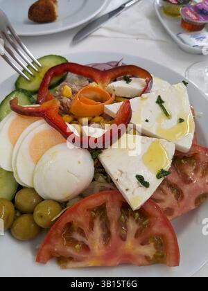 Ein bunter Salat auf einem weißen Teller, mit Tomaten, Oliven, Eiern, Käse, und Paprika, ist bereit, mit einer Gabel genossen zu werden. Stockfoto