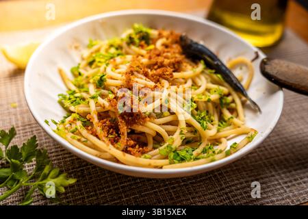 Nahaufnahme des hausgemachten italienischen Gerichts „Pasta con le Sarde“ auf Holztisch, hergestellt aus Spaghetti, Sardinen, Petersilie, Pinienkernen und Brotkrumen. Klassisches ita Stockfoto