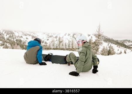Jungs sitzen auf verschneiten Pisten und sind bereit, bergab zu Snowboarden Stockfoto