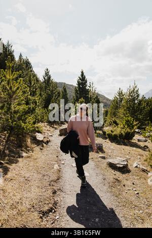 Frau, die durch sonnendurchfluteten Waldweg wandert Stockfoto